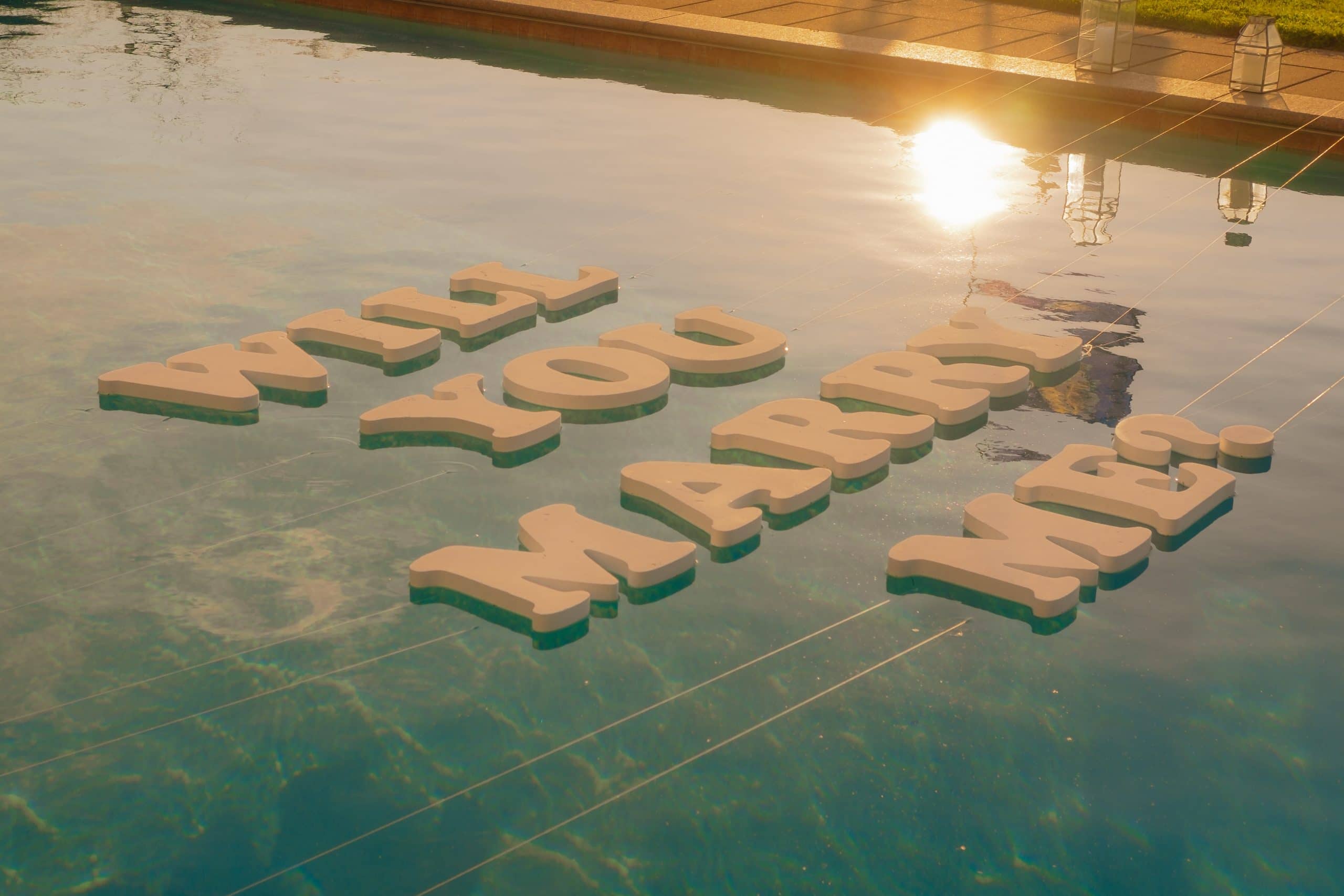 Big letters Will You Marry Me on pool in sunset. Creative way of proposal