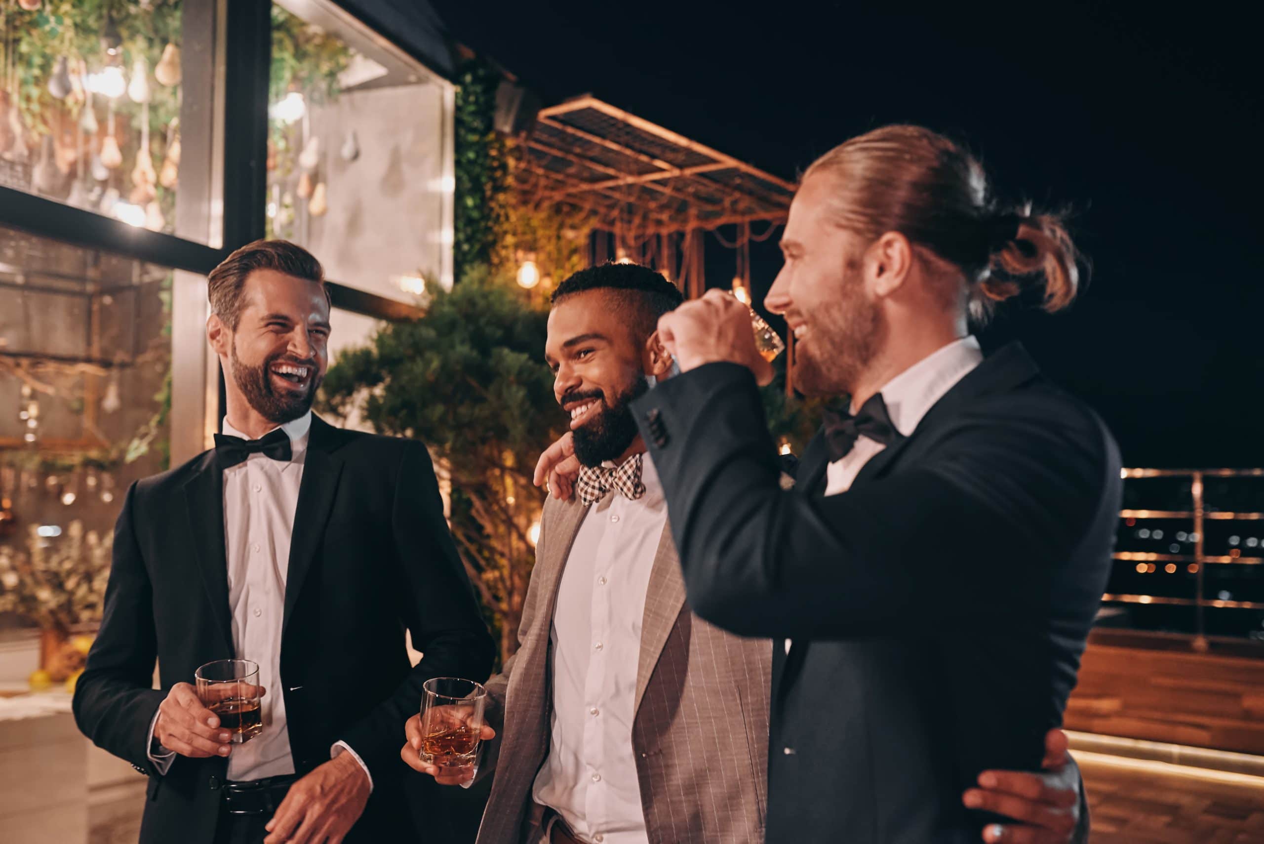 Three happy men in suits holding glasses with whiskey while spen