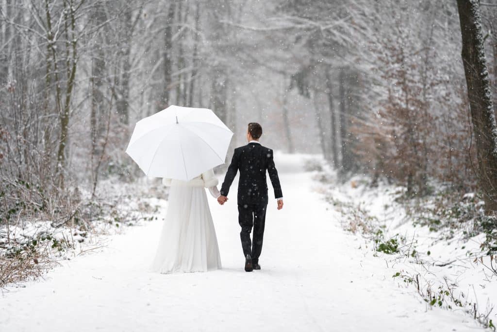 newlyweds in wedding dresses in the winter snowy forest on a walk with an umbrella.