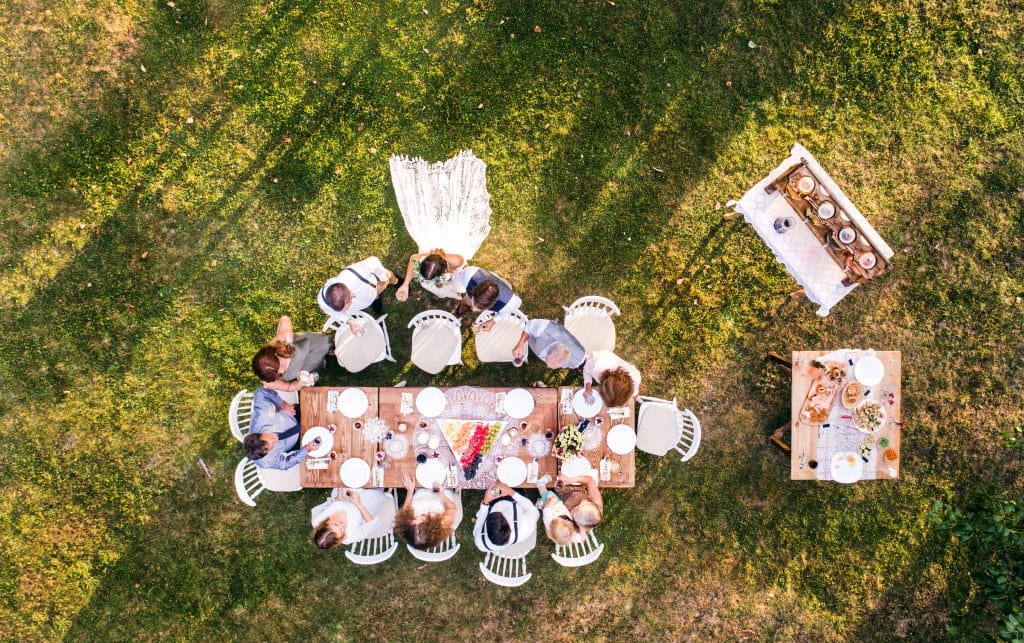 Wedding reception outside in the backyard. Bride and groom with a family standing around the table. Aerial view.
