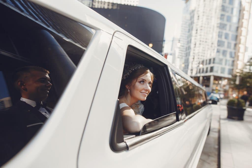 Elegant bride sitting in a white car. Couple in a big town