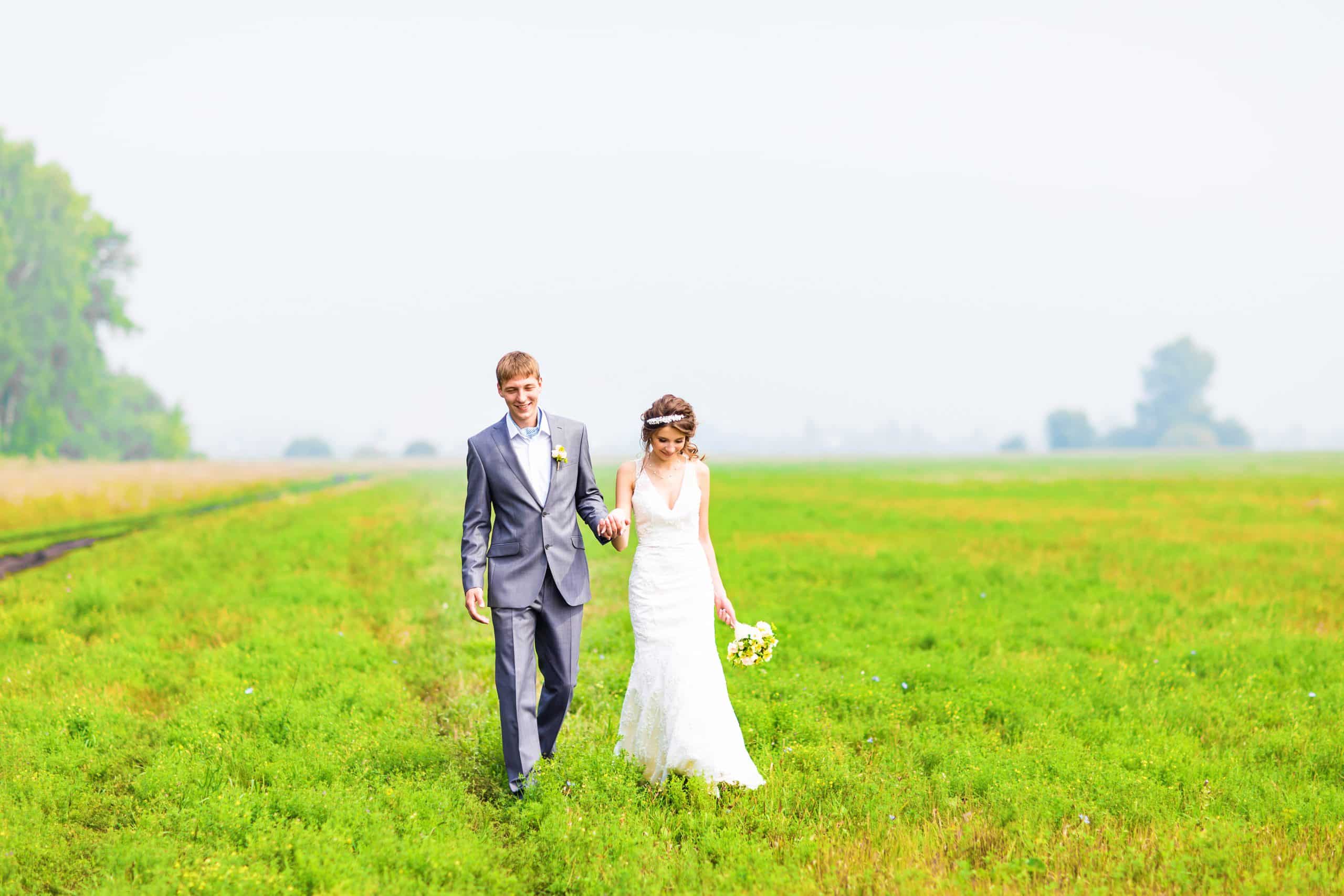 A young couple in love bride and groom, wedding day in summer. Enjoy a moment of happiness and love in a  field. Bride in a luxurious wedding dress on a background bright blue sky with clouds