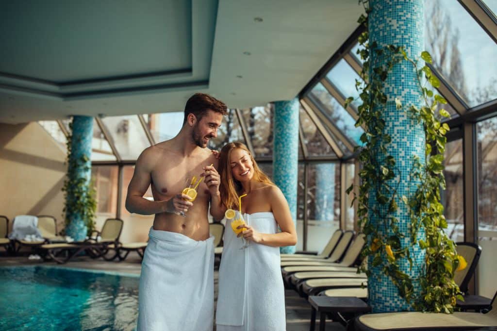 Ein Pärchen mit jeweils einem Cocktail in der Hand im Urlaub am Schwimmbecken