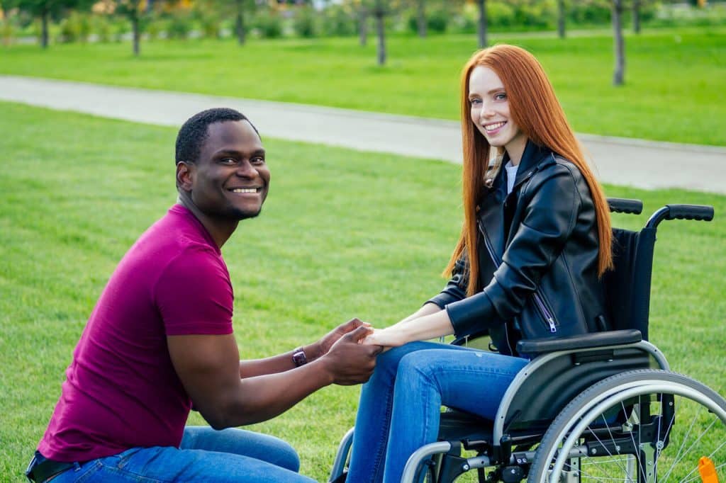Ein Afroamerikaner hält die Hände seiner Partnerin, die im Rollstuhl sitzt.