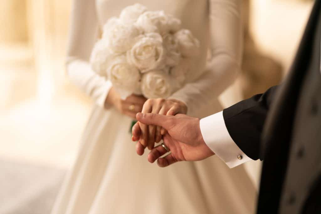 Braut mit weißen Rosen hält die Hand ihres Bräutigams