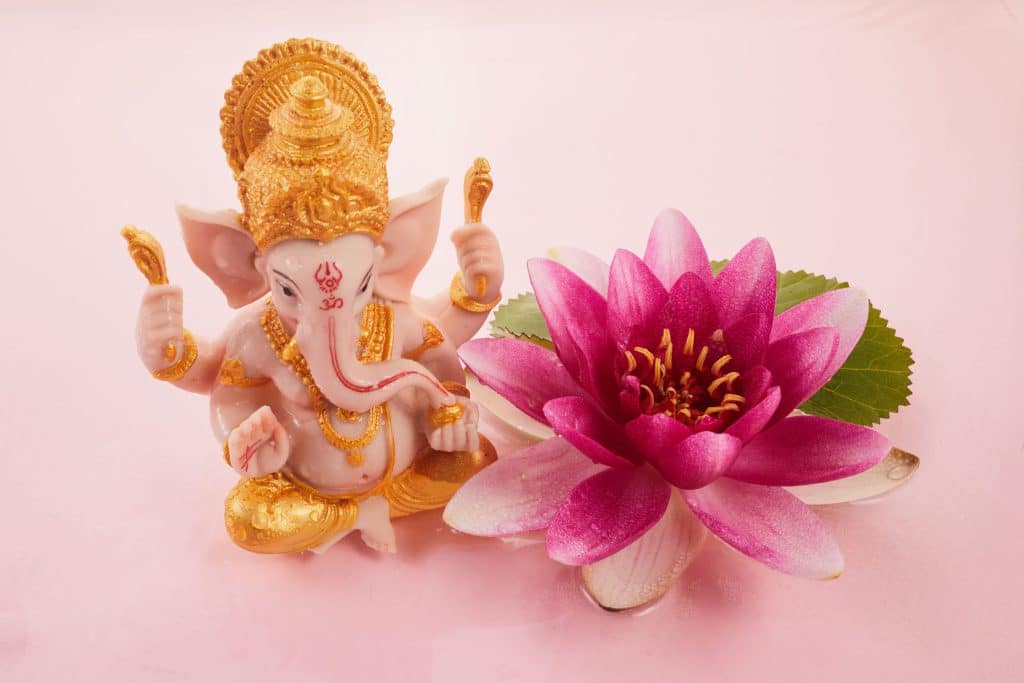 Der hinduistische Gott Ganesha links neben einer lilafarbenen Wasserlilie
