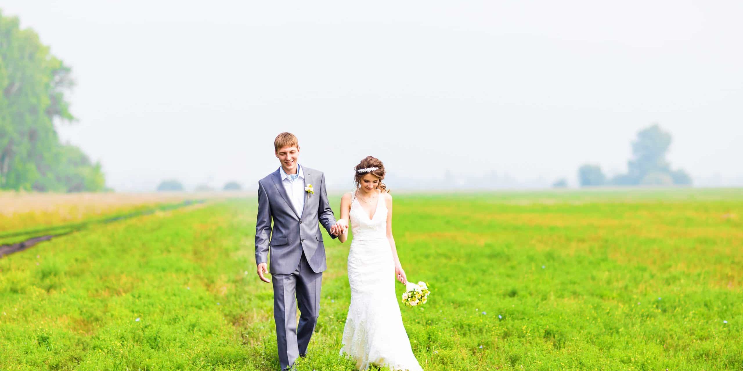A young couple in love bride and groom, wedding day in summer. Enjoy a moment of happiness and love in a  field. Bride in a luxurious wedding dress on a background bright blue sky with clouds