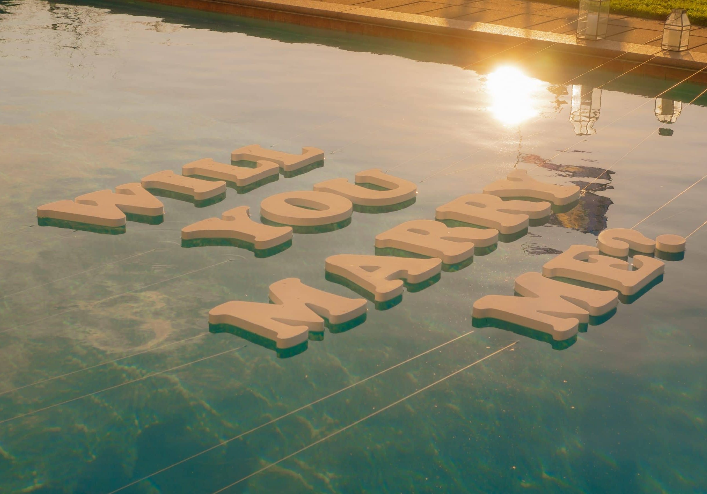 Big letters Will You Marry Me on pool in sunset. Creative way of proposal