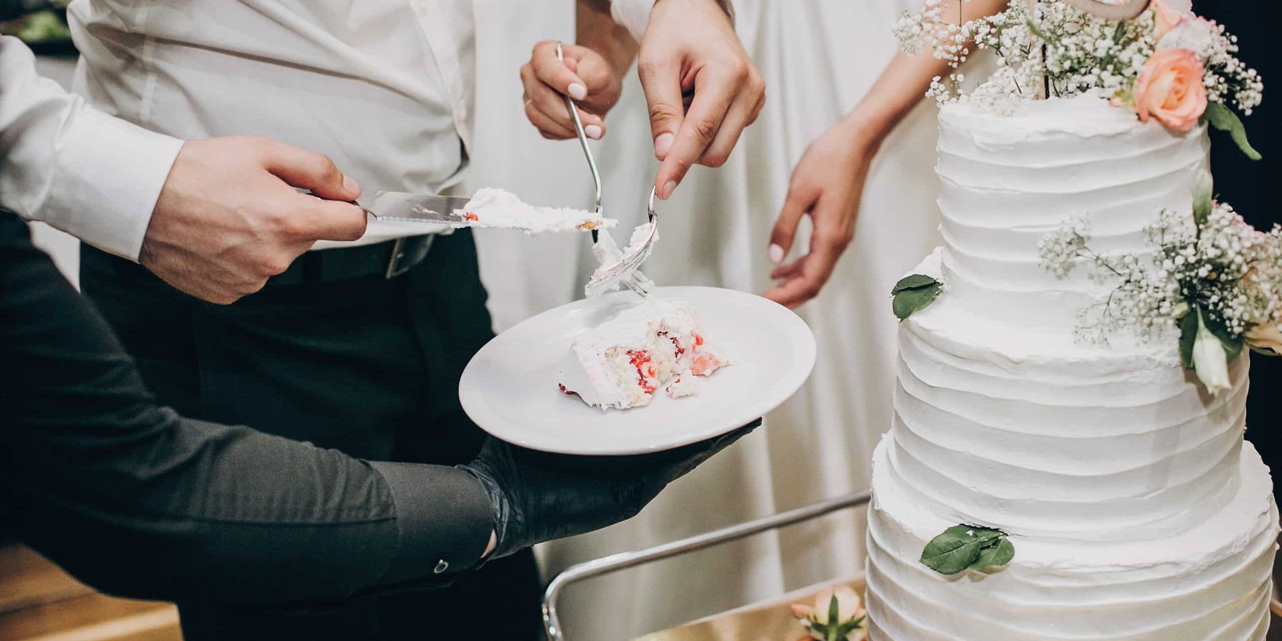 Bride and groom cutting stylish wedding cake at wedding reception in restaurant. Wedding couple holding slice of  wedding cake decorated with flowers