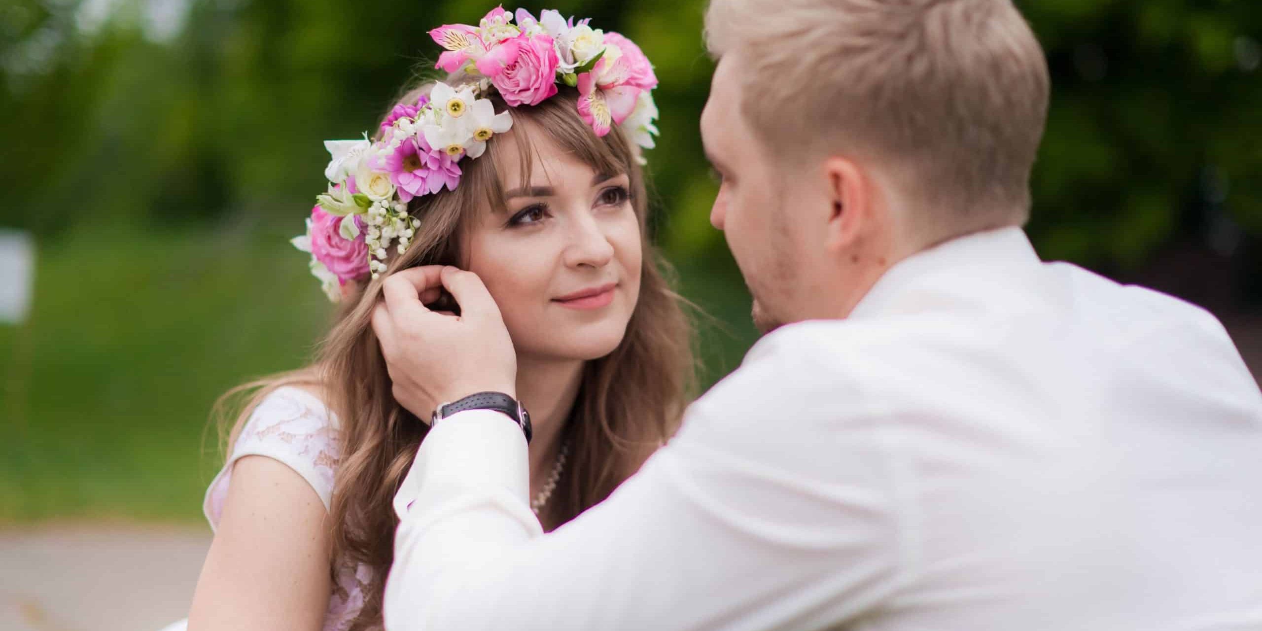 Ein Mann im weißen Hemd strecht über die Wange seiner Freundin mit Blumenhaarkranz