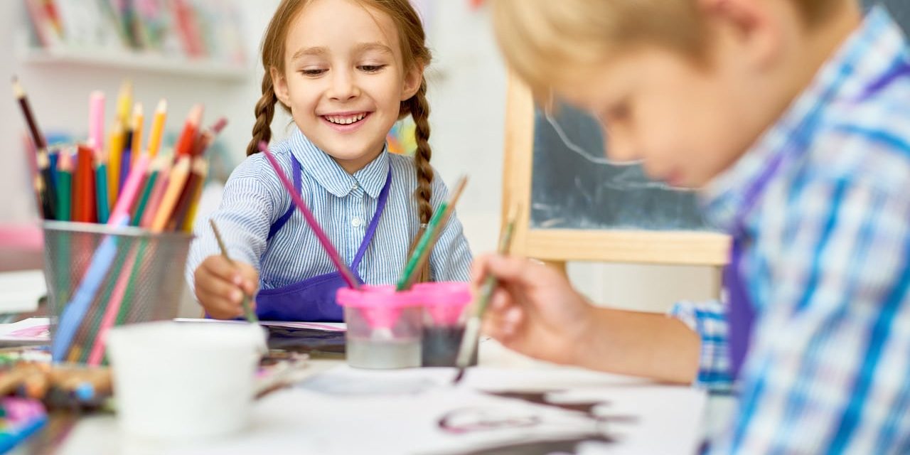 ein Junge und ein Mädchen im Kindergartenalter malen zusammen am Maltisch.