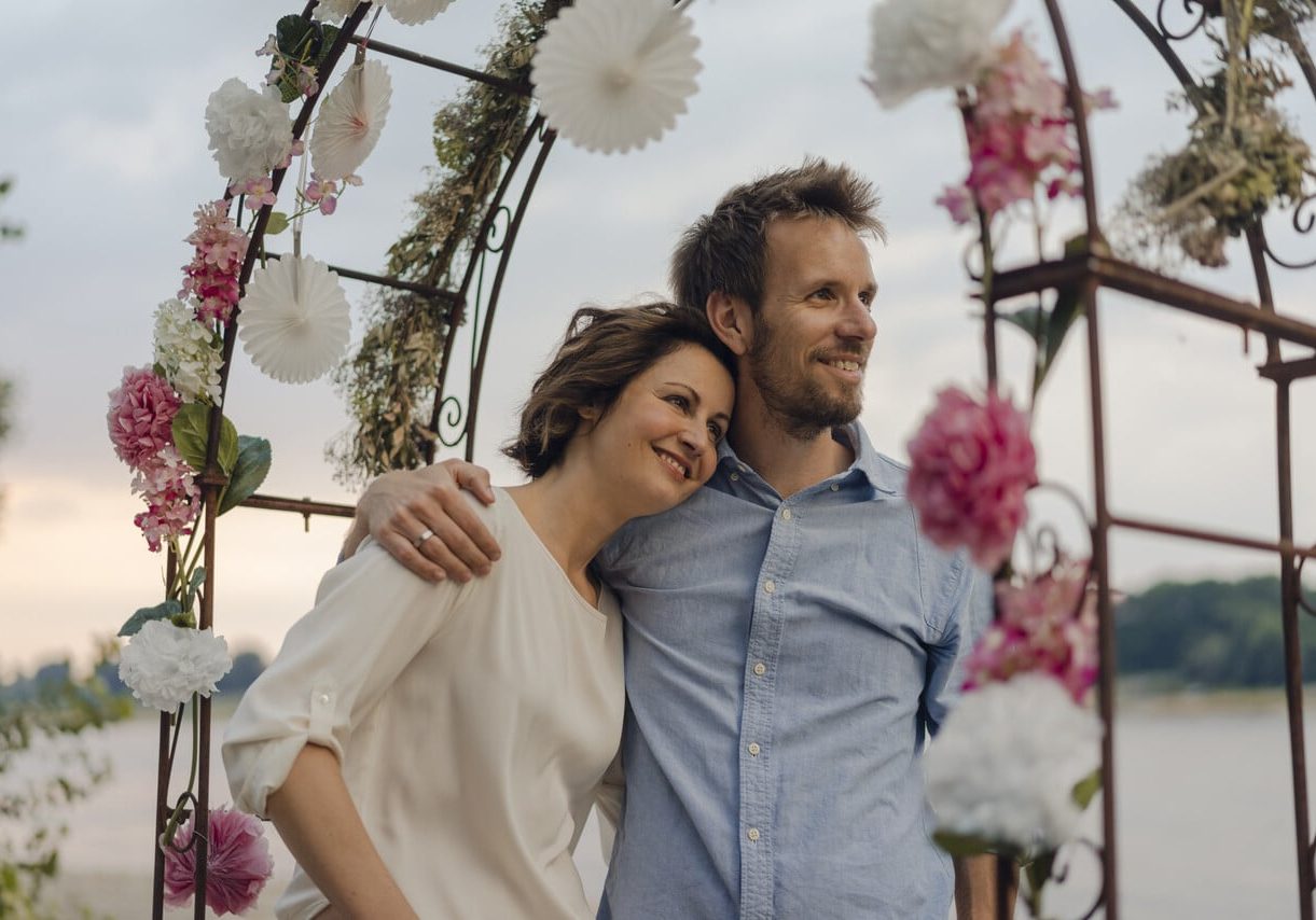 Paar steht unter Blumenbehangendem Hochzeitstorbogen