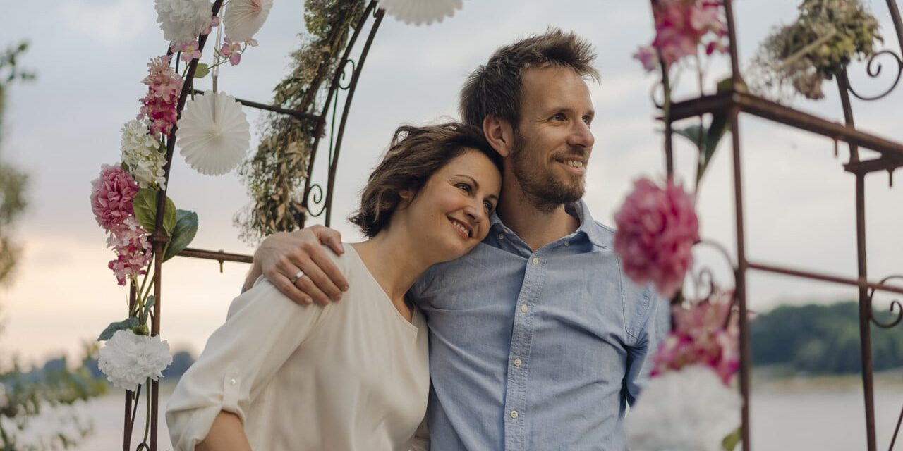 Paar steht unter Blumenbehangendem Hochzeitstorbogen