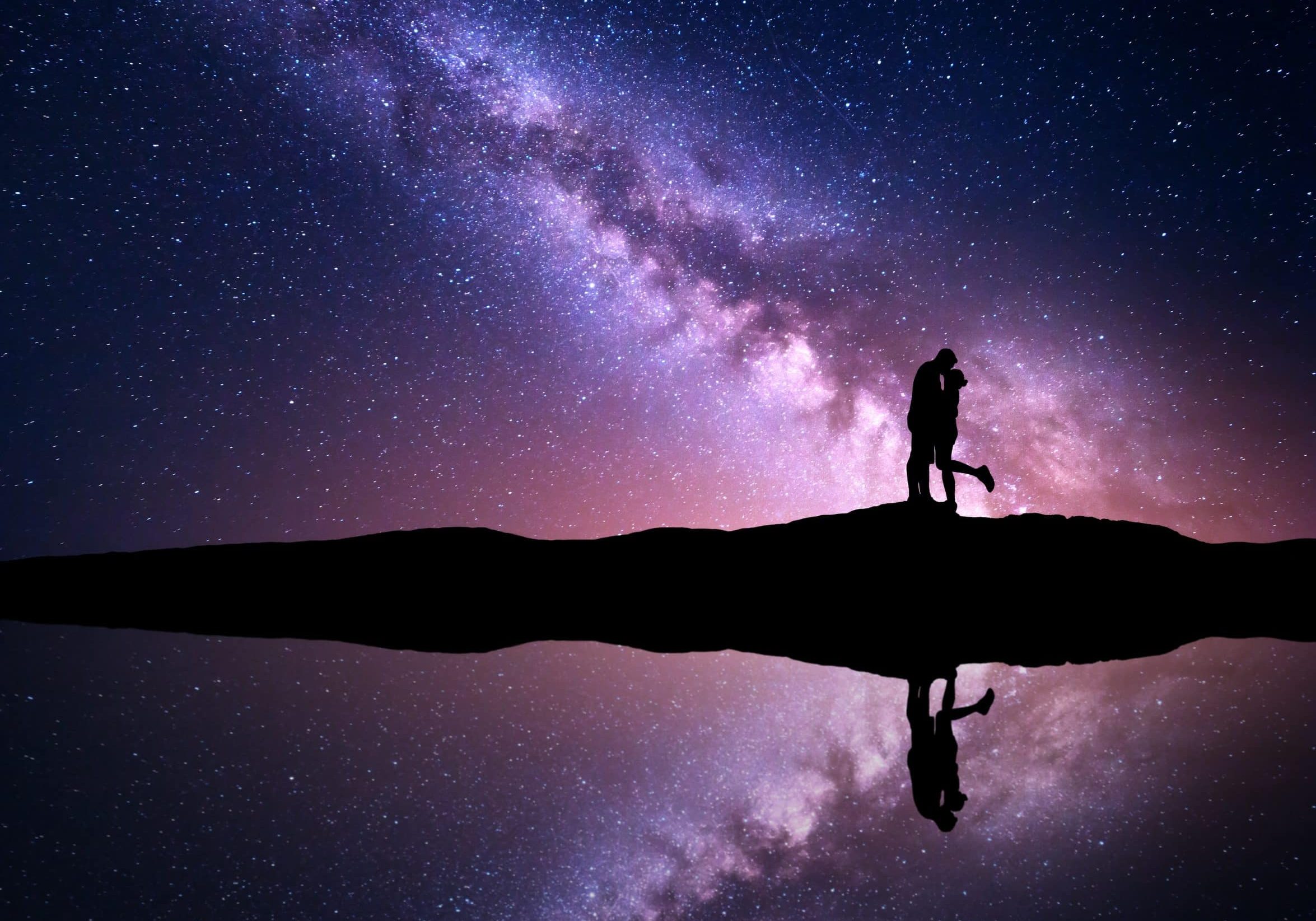 Milky Way. Night landscape with silhouettes of hugging and kissing man and woman on the mountain near the river with sky reflection in water. Starry sky. Lovers. Couple. Purple milky way with people