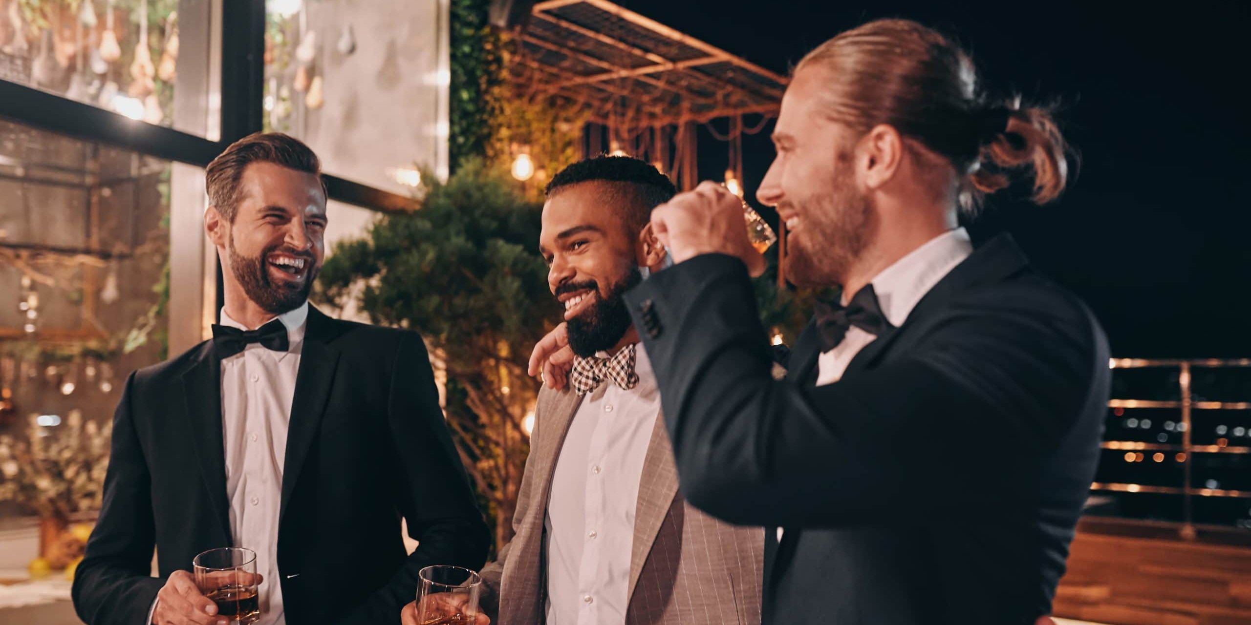 Three happy men in suits holding glasses with whiskey while spen
