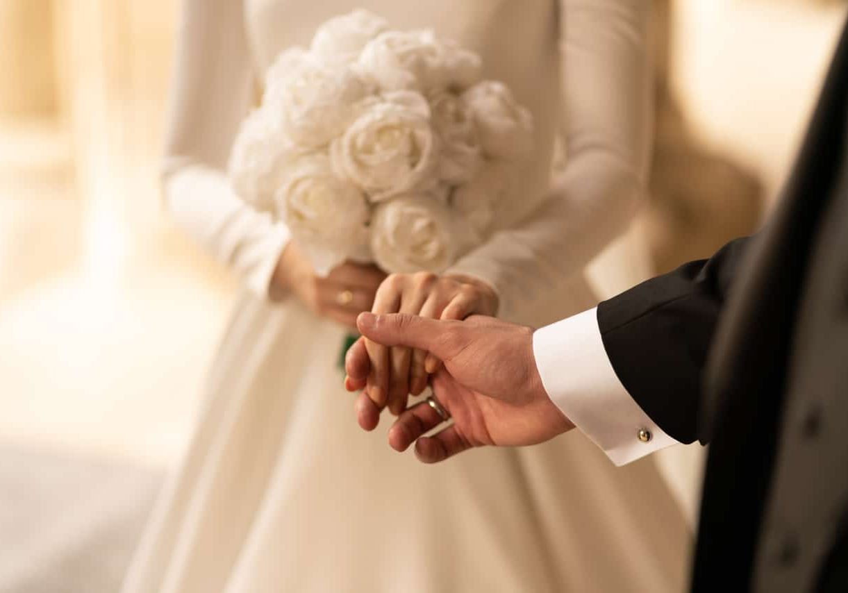 Braut mit weißen Rosen hält die Hand ihres Bräutigams