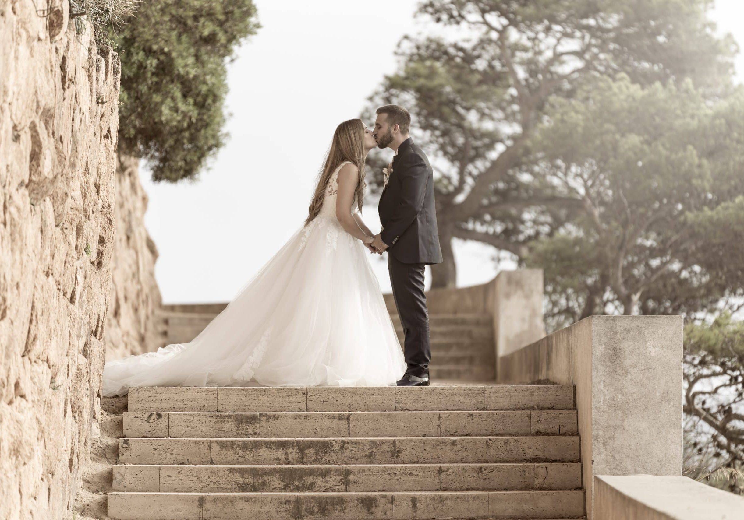 Wedding couple kissing and hugging on stairs with green trees on the background